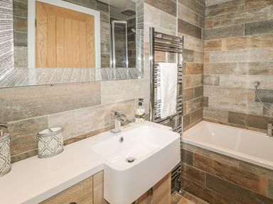 A bathroom with a sink counter a bathtub towel rack and a mirror at River Cottage in Morpeth