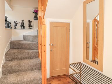 A staircase with carpet and wooden railing next to a wooden door and a wall mirror with a metal shoe rack below at River Cottage in Morpeth