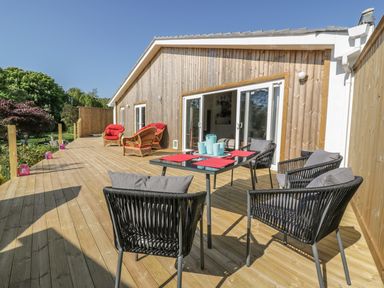 A wooden deck with black chairs and a table with turquoise vases and red placemats outside a wood-paneled house at Chy Lagen Hos in Newquay