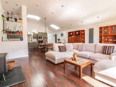An open plan living room and kitchen with beige sectional sofa wooden coffee table dining table and wooden cabinets at Chy Lagen Hos in Newquay