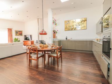 An open plan kitchen and dining area with a round wooden table and chairs a white sofa and a wood stove at Chy Lagen Hos in Newquay