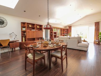A dining area with a round wooden table set with plates and glasses next to a beige sofa in a living room with wooden furniture at Chy Lagen Hos in Newquay