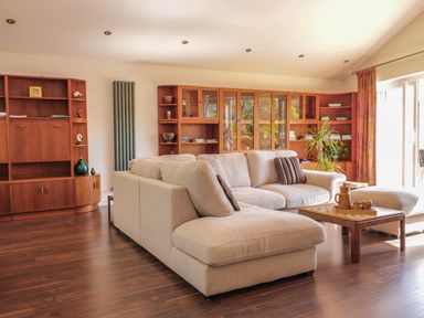 A living room with a beige sectional sofa wooden shelves and a coffee table at Chy Lagen Hos in Newquay