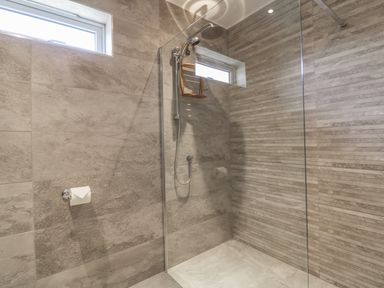 A walk in shower with tiled walls and two small windows at Chy Lagen Hos in Newquay