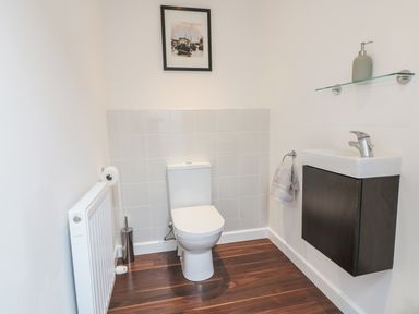 A bathroom with a toilet sink a towel ring with towel a soap dispenser on a glass shelf and a radiator at Chy Lagen Hos in Newquay