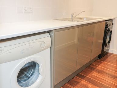 A utility room with a washing machine sink and cabinets at Chy Lagen Hos in Newquay