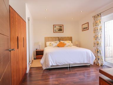 A bedroom with a bed a bedside table lamps wooden wardrobes and floral curtains at Chy Lagen Hos in Newquay