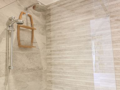 A tiled shower area with two showerheads and a wooden shower caddy at Chy Lagen Hos in Newquay