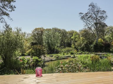 A garden with pond and plants viewed from a wooden deck with a pink lantern at Chy Lagen Hos in Newquay