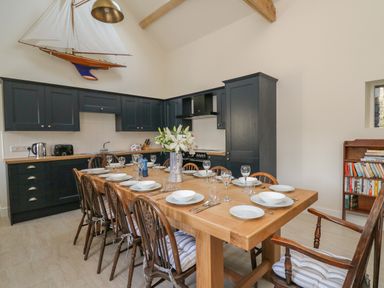 A kitchen with dark cabinets and a wooden dining table set with plates and glasses at The Old Carriage Court in Kidwelly
