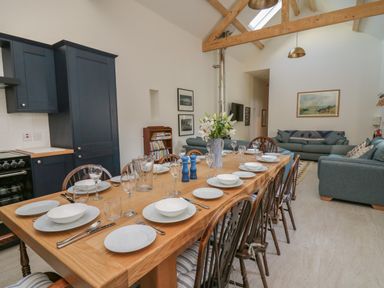 A dining area with a wooden table set with plates and glasses next to a seating area with sofas and framed pictures at The Old Carriage Court in Kidwelly