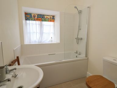 A bathroom with a bathtub shower combo sink and toilet with wooden seat at The Old Carriage Court in Kidwelly