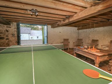 A room with a ping pong table wooden chairs and a wooden table with games at The Old Carriage Court in Kidwelly