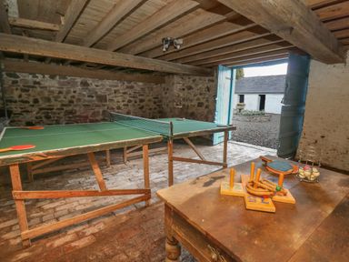 A room with a ping pong table and a wooden table with game equipment near open blue doors at The Old Carriage Court in Kidwelly