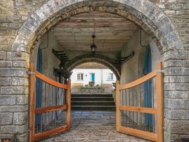An open wooden gate in a stone archway leading to steps and a building with blue doors at The Old Carriage Court in Kidwelly
