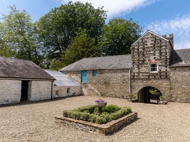 A stone courtyard with a small garden bed and historic stone buildings at The Old Carriage Court in Kidwelly