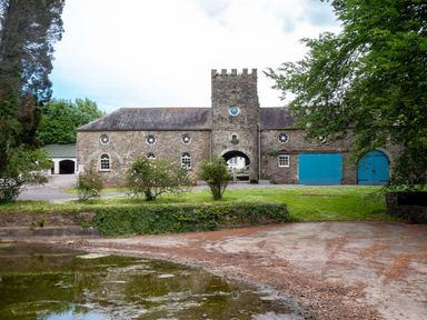 A stone building with blue doors and round windows beside a pond at The Old Carriage Court in Kidwelly