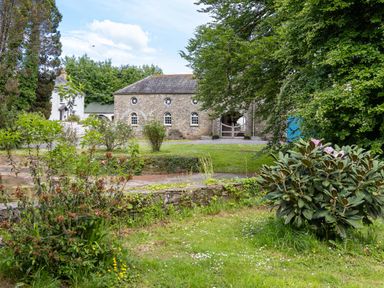 A garden with bushes and grass and stone buildings in the background at The Old Carriage Court in Kidwelly