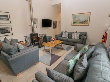A sitting room with three sofas a wooden coffee table a rug a wall mounted tv a wood burning stove and framed pictures at The Old Carriage Court in Kidwelly