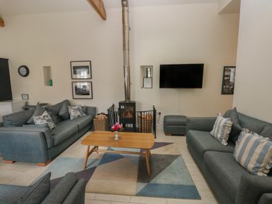 A living room with two sofas a wooden coffee table a fireplace and a wall-mounted TV at The Old Carriage Court in Kidwelly