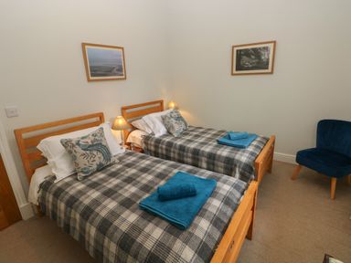 A bedroom with two single beds with checkered blankets and blue towels a bedside lamp two framed pictures and a blue chair at The Old Carriage Court in Kidwelly