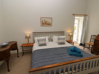 A bedroom with a bed with blue blanket and folded towels bedside tables and lamps a chair a dresser and a framed picture on the wall at The Old Carriage Court in Kidwelly