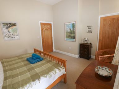 A bedroom with a wooden bed with a green blanket and blue towels on it a dresser with a decorative plate a wicker chair a small chest of drawers with a fan on top and two wooden doors at The Old Carriage Court in Kidwelly