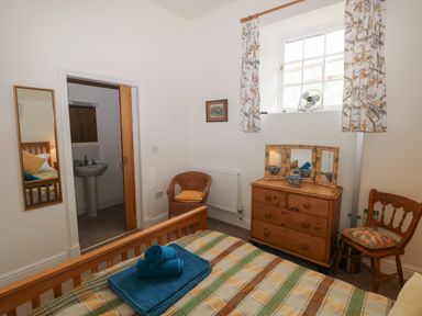 A bedroom with a wooden bed a dresser a wicker chair and a window with floral curtains at The Old Carriage Court in Kidwelly