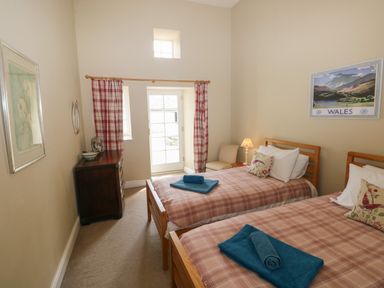 A bedroom with two single beds with checkered bedspreads and blue towels at The Old Carriage Court in Kidwelly