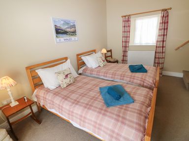 A bedroom with two single beds with plaid bedcovers blue towels bedside tables lamps and a window with plaid curtains at The Old Carriage Court in Kidwelly