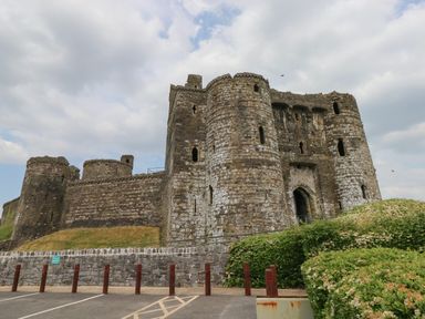 An exterior view of a stone castle with round towers and an arched entrance at The Old Carriage Court in Kidwelly