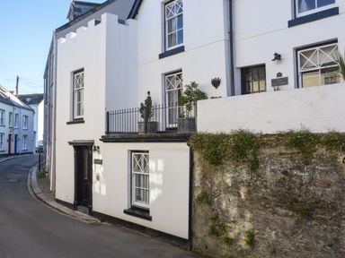 A street view of white houses with black doors and windows and a stone wall with plants at Serendipity in Fowey