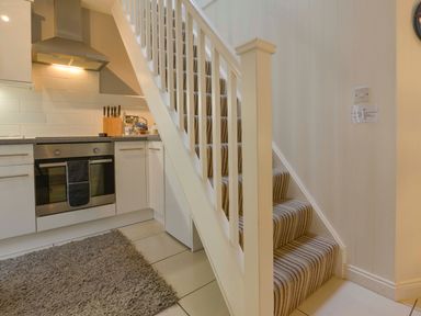A kitchen area with a built-in oven and stove next to carpeted stairs with a striped pattern at Serendipity in Fowey