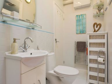 A bathroom with a sink, toilet, towel rack, storage basket unit, and decorative wall art at Serendipity in Fowey