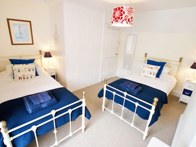 A bedroom with two single beds blue bedding and folded towels at The Shell Seekers in Fowey