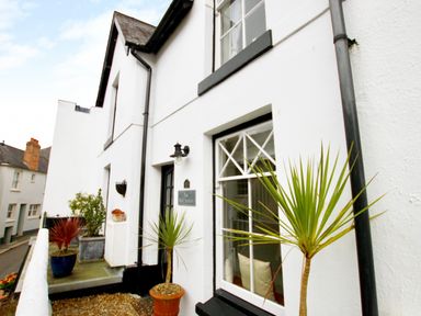 Exterior view of a white house with potted plants near the window and door at The Shell Seekers in Fowey