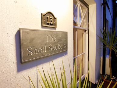 A house wall with a number 13 and a sign reading The Shell Seekers next to a window and plants at The Shell Seekers in Fowey