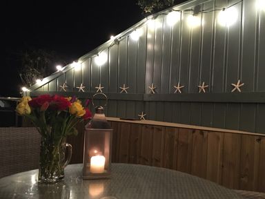 A patio table with a flower vase and a candle lantern next to a fence with starfish and string lights at The Shell Seekers in Fowey