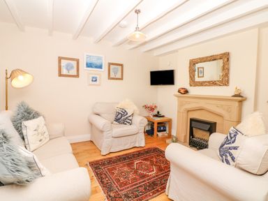 A living room with sofas and armchairs around a fireplace with a mirror above at The Shell Seekers in Fowey