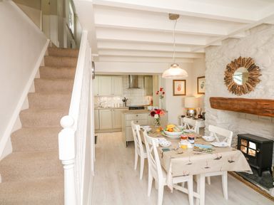 A dining area with a table set for breakfast next to a staircase and a kitchen at The Shell Seekers in Fowey