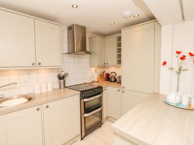 A kitchen with cream cabinets stove kettle and red flowers on a counter at The Shell Seekers in Fowey