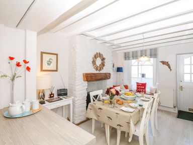 A dining area with a table set for breakfast and a white stone fireplace in the background at The Shell Seekers in Fowey