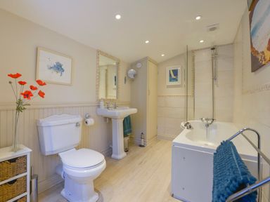 A bathroom with a toilet sink bathtub and flowers on a small cabinet at The Shell Seekers in Fowey