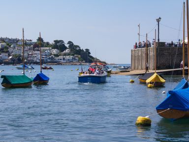 A harbor with sailboats and a motorboat with people near a stone quay and houses in the background at The Shell Seekers in Fowey