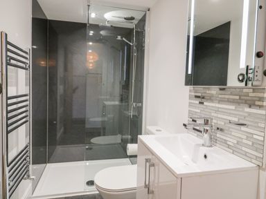 A bathroom with a shower enclosure, toilet, sink, and a mirrored cabinet with tiled backsplash at Cefn Nannau in Ty-nant near Cerrigydrudion