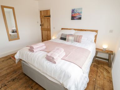 A bedroom with a double bed with white bedding and pink towels with a wooden door mirror and bedside table with a lamp at Cefn Nannau in Ty-nant near Cerrigydrudion