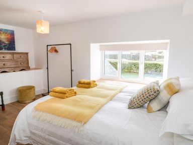 A bedroom with a bed with yellow blankets and pillows a window chest of drawers and a clothing rack at Cefn Nannau Ty-nant near Cerrigydrudion