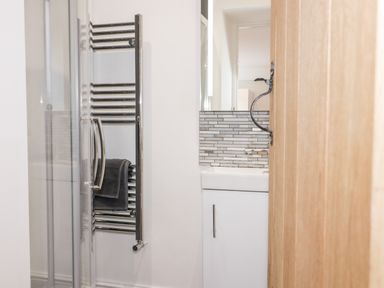 A bathroom with a glass shower door a chrome towel radiator a sink with cabinet and tiled backsplash at Cefn Nannau in Ty-nant near Cerrigydrudion