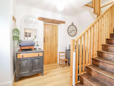 A hallway with a wooden door a vintage cabinet with folded blankets a mirror a clock a small chair and wooden stairs at Cefn Nannau in Ty-nant near Cerrigydrudion