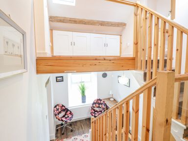 A stairway area with wooden railings overlooking a small seating space with two floral chairs and a window at Cefn Nannau in Ty-nant near Cerrigydrudion
